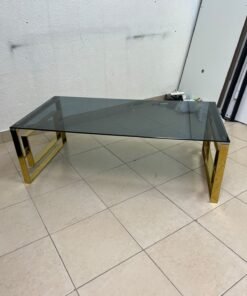 A modern coffee table featuring a dark glass top (tempered or smoked glass) and a shiny gold metal frame and base, distinguished by an interlocking geometric design on the sides. - Image 7