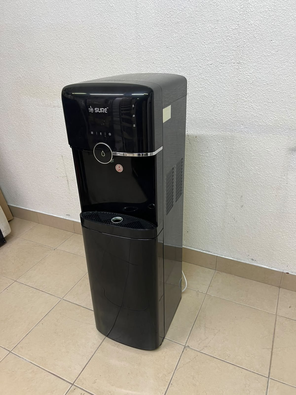 A black, freestanding water cooler from Sure—specifically a bottom-loading model (such as the SBL70 or SBL1970BP)—that allows the water bottle to be easily placed inside the bottom compartment.