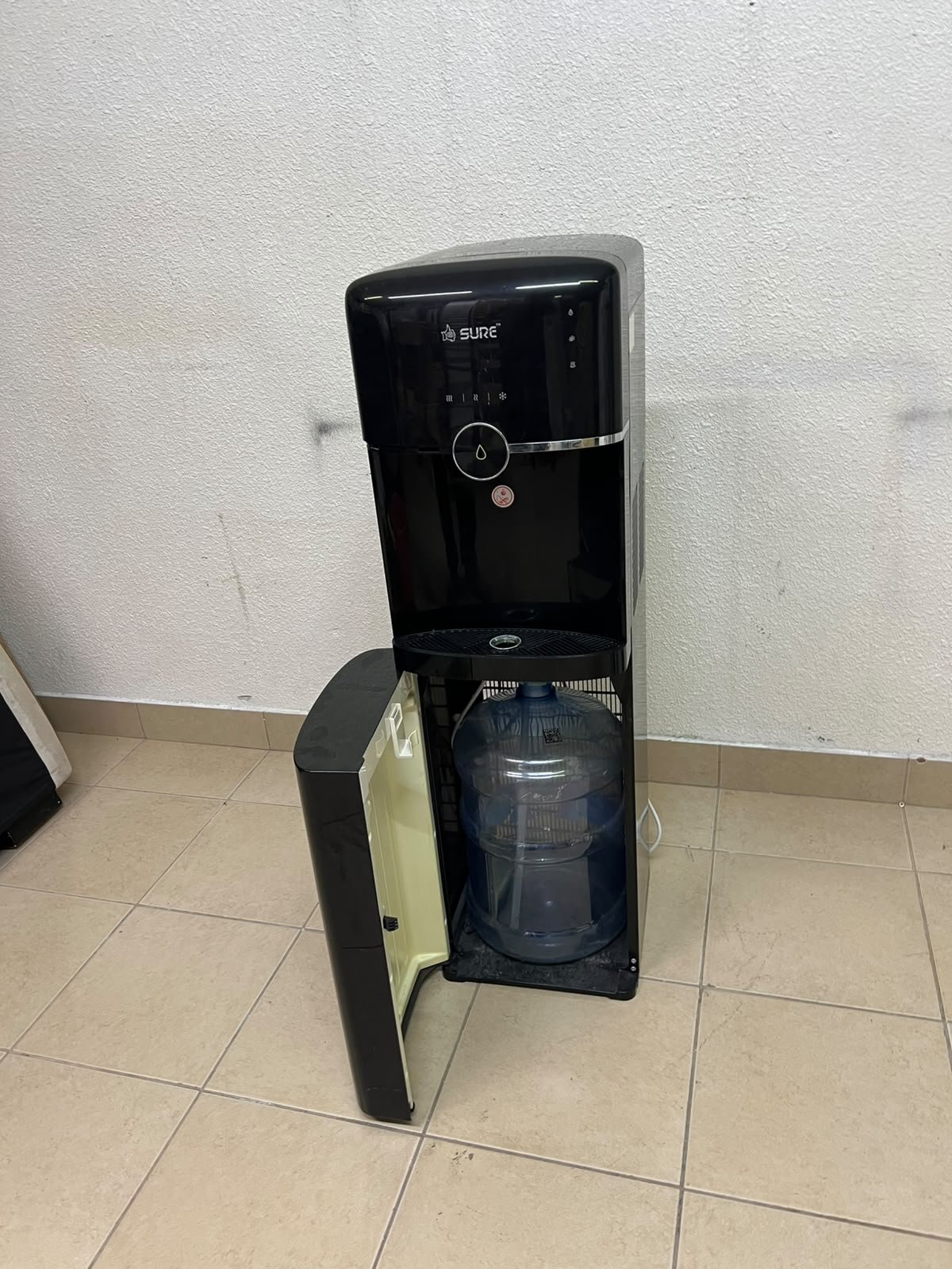 A black, freestanding water cooler from Sure—specifically a bottom-loading model (such as the SBL70 or SBL1970BP)—that allows the water bottle to be easily placed inside the bottom compartment. - Image 9