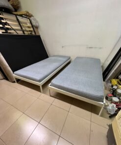 Two single beds with white metal frames, featuring lightweight foam mattresses in a light gray/blue color—similar to the ÅGOTNES foam mattress from IKEA.