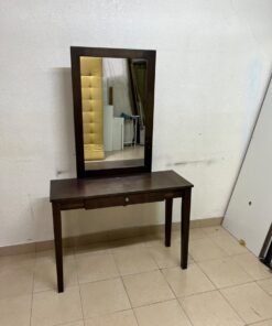 A dark brown (espresso) wooden vanity table with a minimalist design, featuring a rectangular surface, a small central drawer, and an upright vertical mirror set within a tall wooden frame.