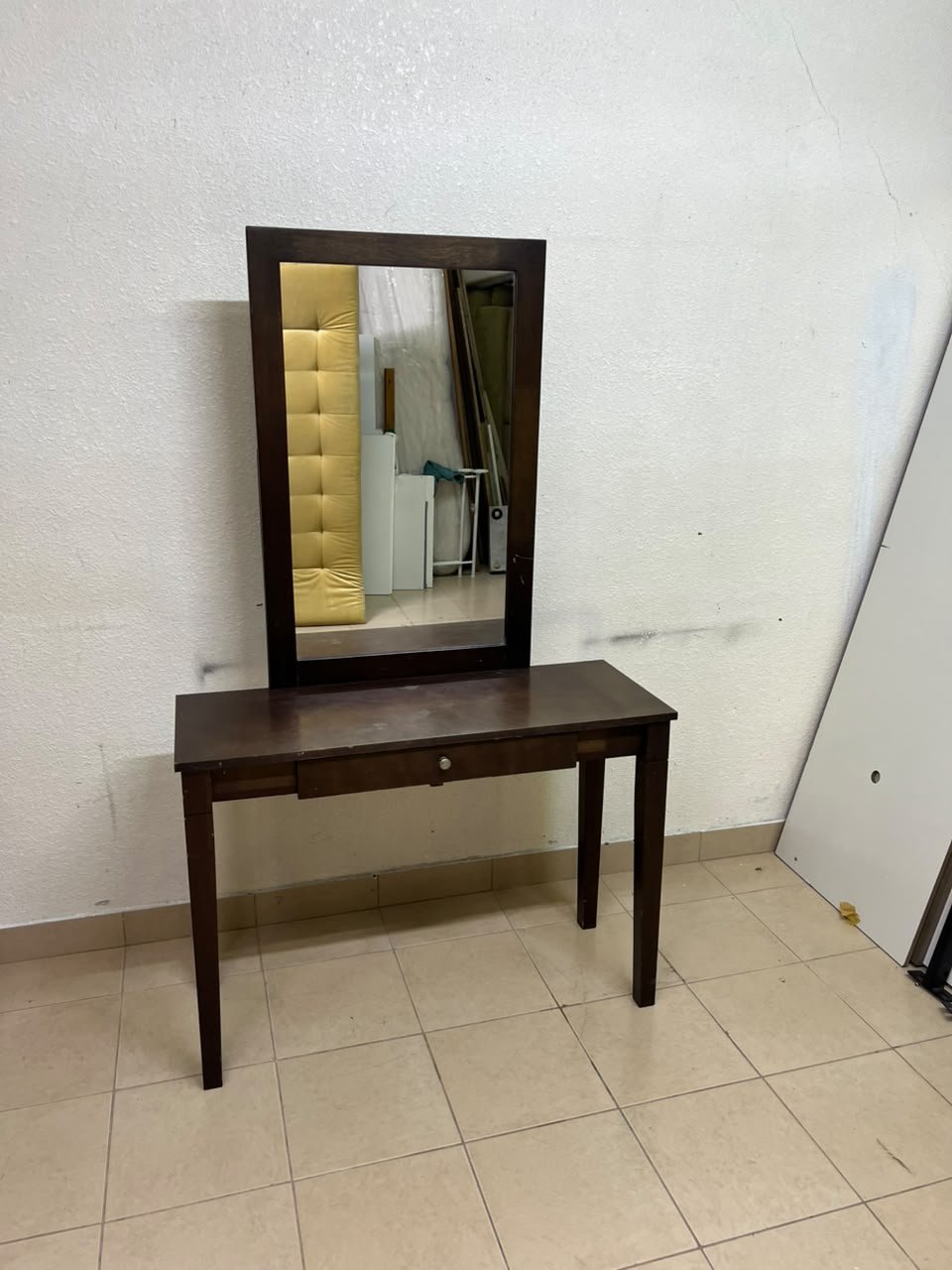 A dark brown (espresso) wooden vanity table with a minimalist design, featuring a rectangular surface, a small central drawer, and an upright vertical mirror set within a tall wooden frame.