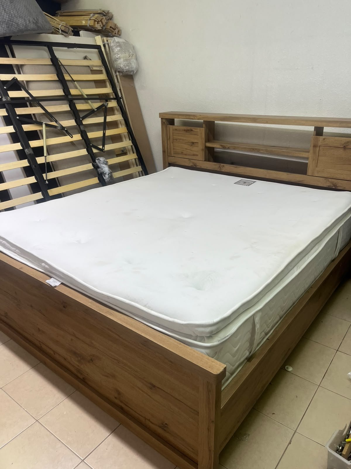 A modern-style wooden double bed (king or queen size) with a mattress, featuring a headboard equipped with shelves and storage cabinets—from Home Centre.