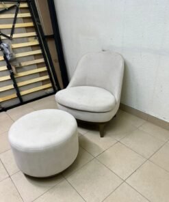 An armchair (poltrona) with a matching footstool (pouffe), featuring a modern, curved design; upholstered in a light beige velvet or linen-like fabric and set upon elegant wooden legs. - Image 2
