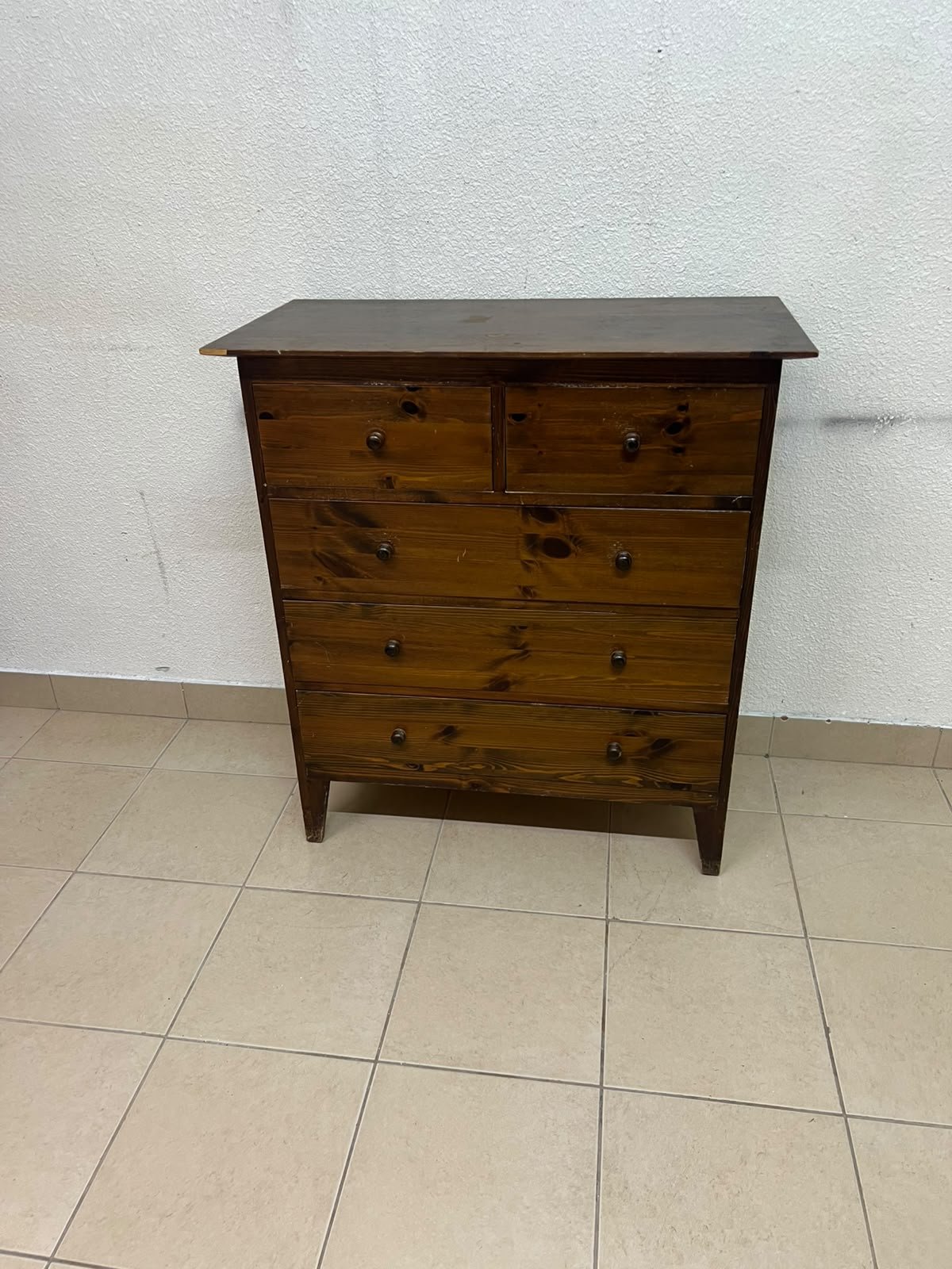 A classic chest of drawers made of solid wood (such as pine or a darker wood), featuring two small drawers at the top and four large, full-width drawers below; it is accented with small, round knobs and elevated wooden legs.