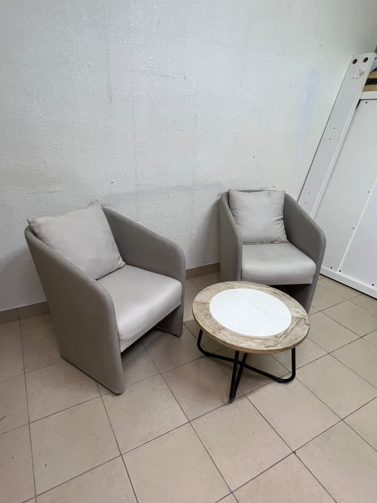 A seating set consisting of two individual grey chairs with square back cushions, with a small, round coffee table—featuring a white top and a black metal base—placed between them. - Image 2