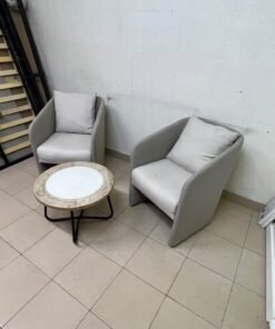 A seating set consisting of two individual grey chairs with square back cushions, with a small, round coffee table—featuring a white top and a black metal base—placed between them.