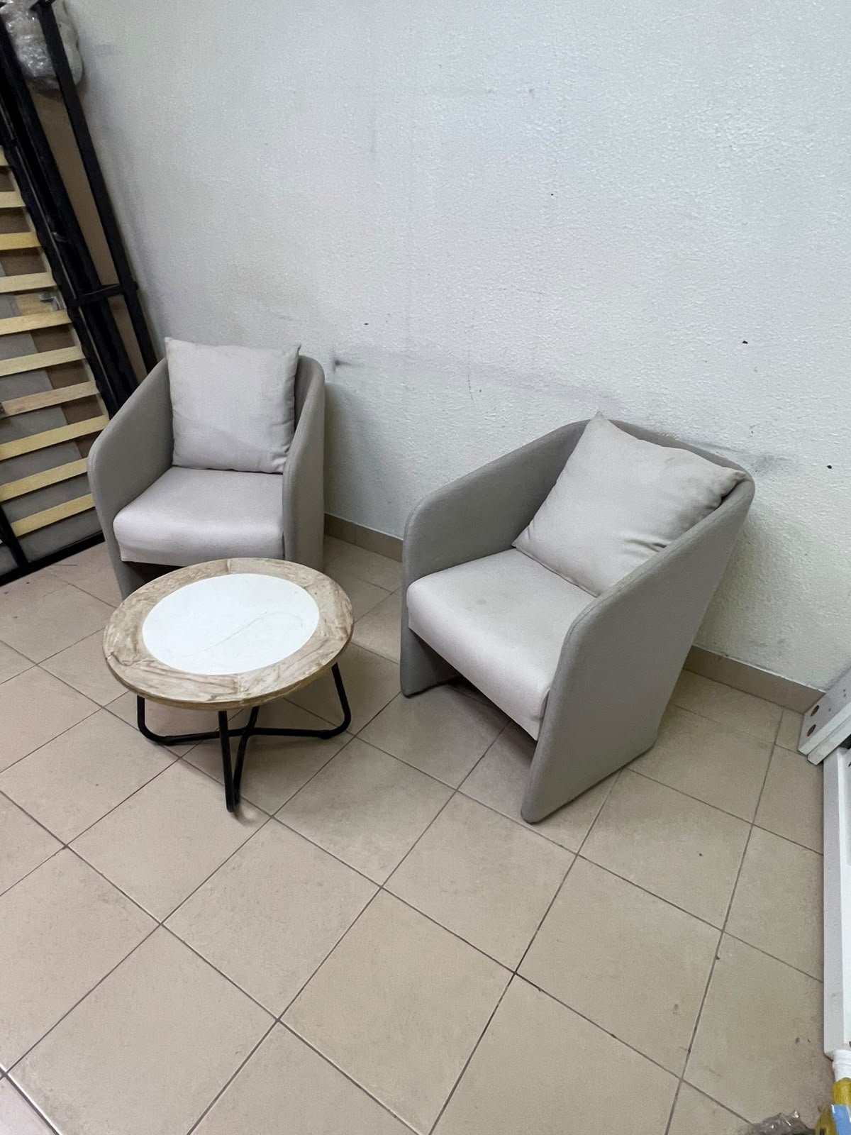 A seating set consisting of two individual grey chairs with square back cushions, with a small, round coffee table—featuring a white top and a black metal base—placed between them.
