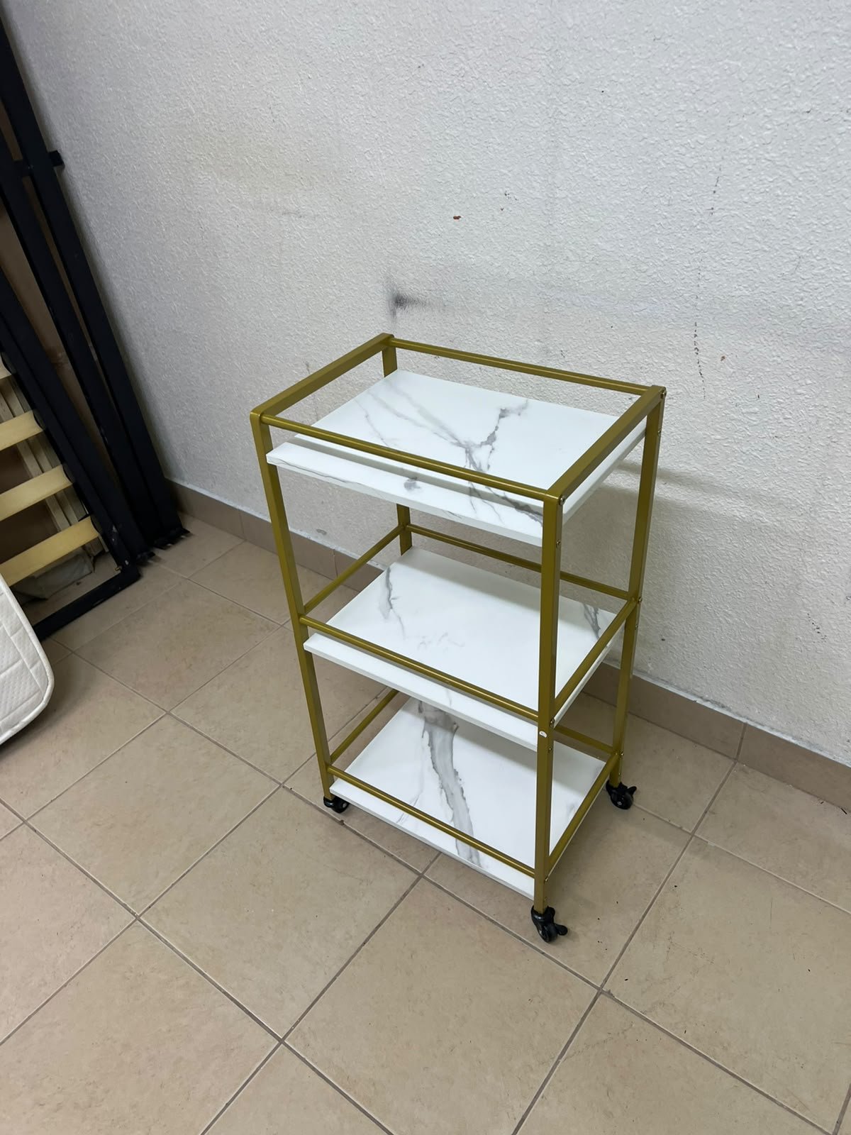 A 3-tier storage or serving cart on wheels, featuring a gold-colored metal frame and white, marble-design shelves. - Image 2