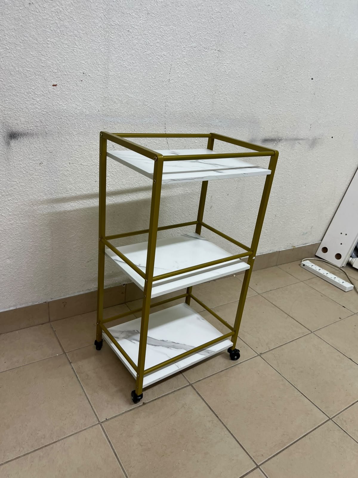 A 3-tier storage or serving cart on wheels, featuring a gold-colored metal frame and white, marble-design shelves. - Image 3