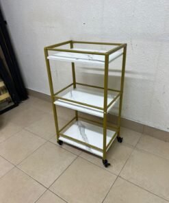 A 3-tier storage or serving cart on wheels, featuring a gold-colored metal frame and white, marble-design shelves.