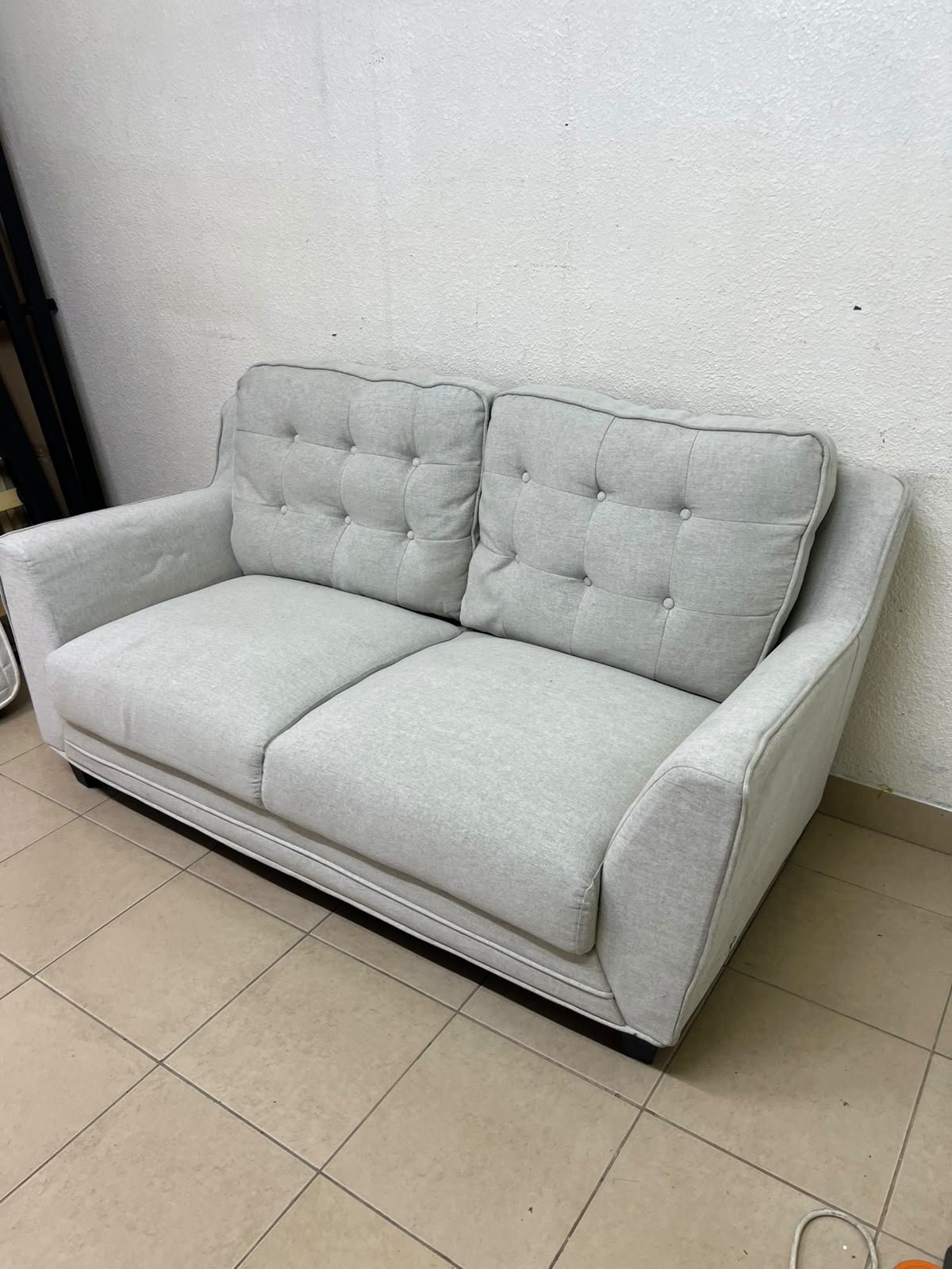 A light gray/beige two-seater fabric sofa featuring button-tufted backrests and short black legs; it closely resembles models such as the Pan Emirates Rosebond two-seater or the Pan Emirates Akli two-seater.