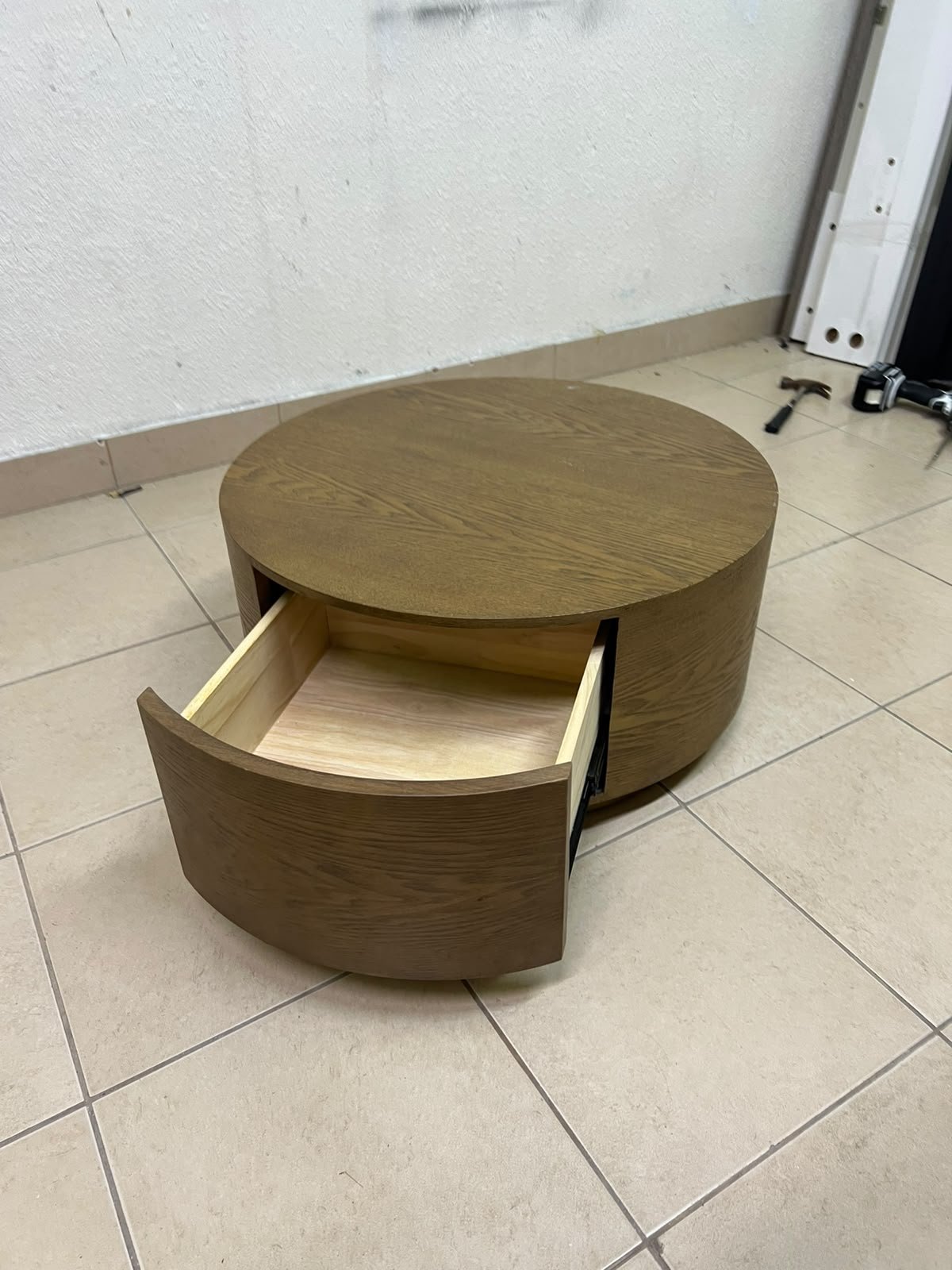 A round, dark oak-colored wooden coffee table, featuring an elegant, modern design with a curved storage drawer equipped with concealed or recessed handles.