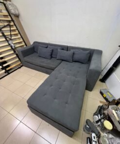 A dark gray L-shaped sectional sofa with a modern design, featuring a long chaise lounge, a tufted seat cushion, and additional back cushions.