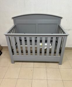 A convertible crib (such as the Serta Barrett model or the Dylan crib by Juniors, available at Centrepoint UAE) in an elegant gray color, featuring a classic, adjustable design that adapts to the various stages of a child's growth.