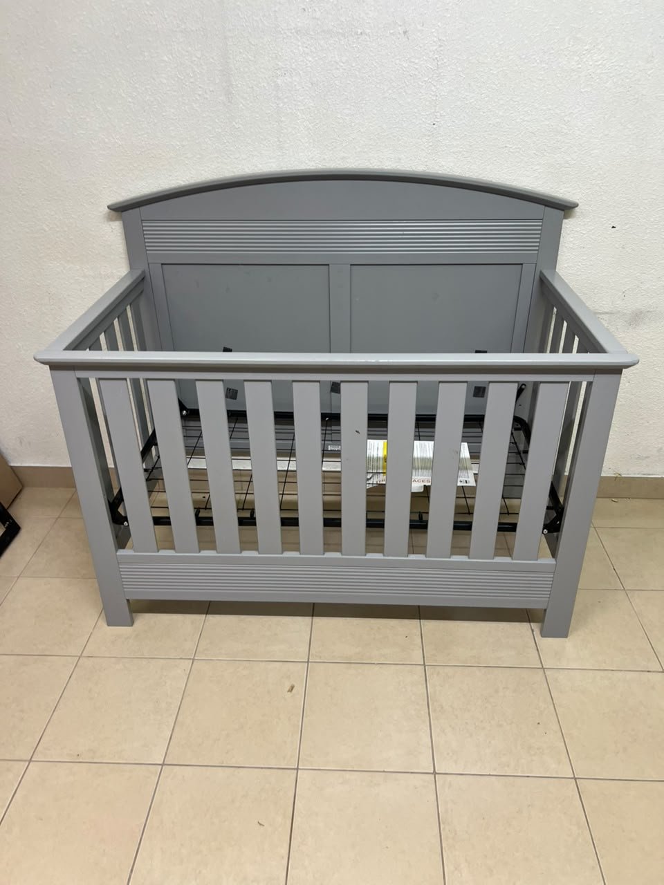 A convertible crib (such as the Serta Barrett model or the Dylan crib by Juniors, available at Centrepoint UAE) in an elegant gray color, featuring a classic, adjustable design that adapts to the various stages of a child's growth.