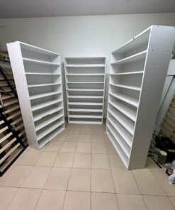 Three white open shelving/display units, constructed from wood, melamine, or MDF, featuring multi-level shelves.