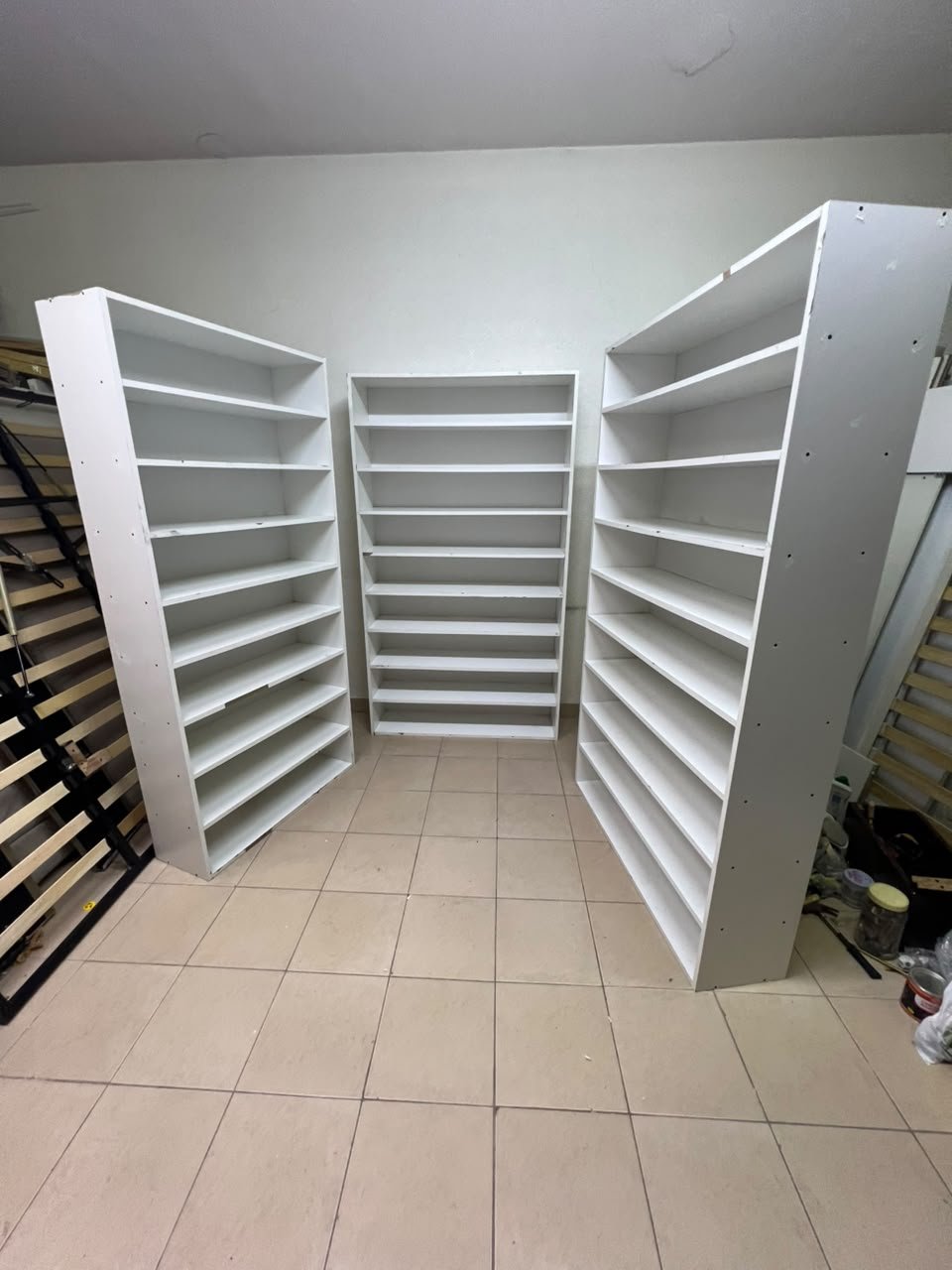 Three white open shelving/display units, constructed from wood, melamine, or MDF, featuring multi-level shelves.