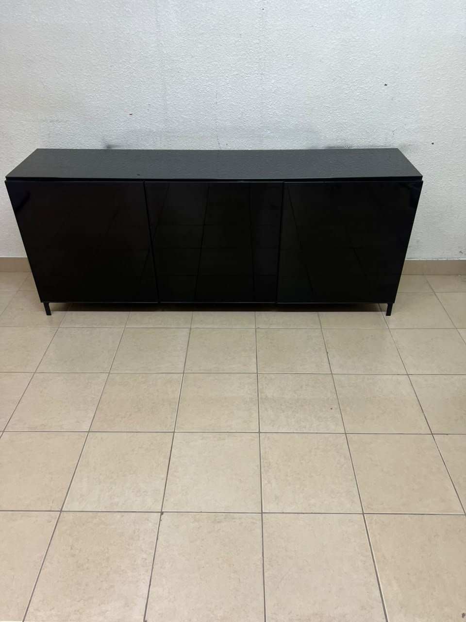 A cabinet (such as a TV stand or sideboard) that appears as a glossy black storage unit with three doors and slender legs; it bears a strong resemblance to the IKEA BESTÅ collection (specifically the Selsviken/Stubbarp combination in black-brown with high-gloss doors). - Image 4