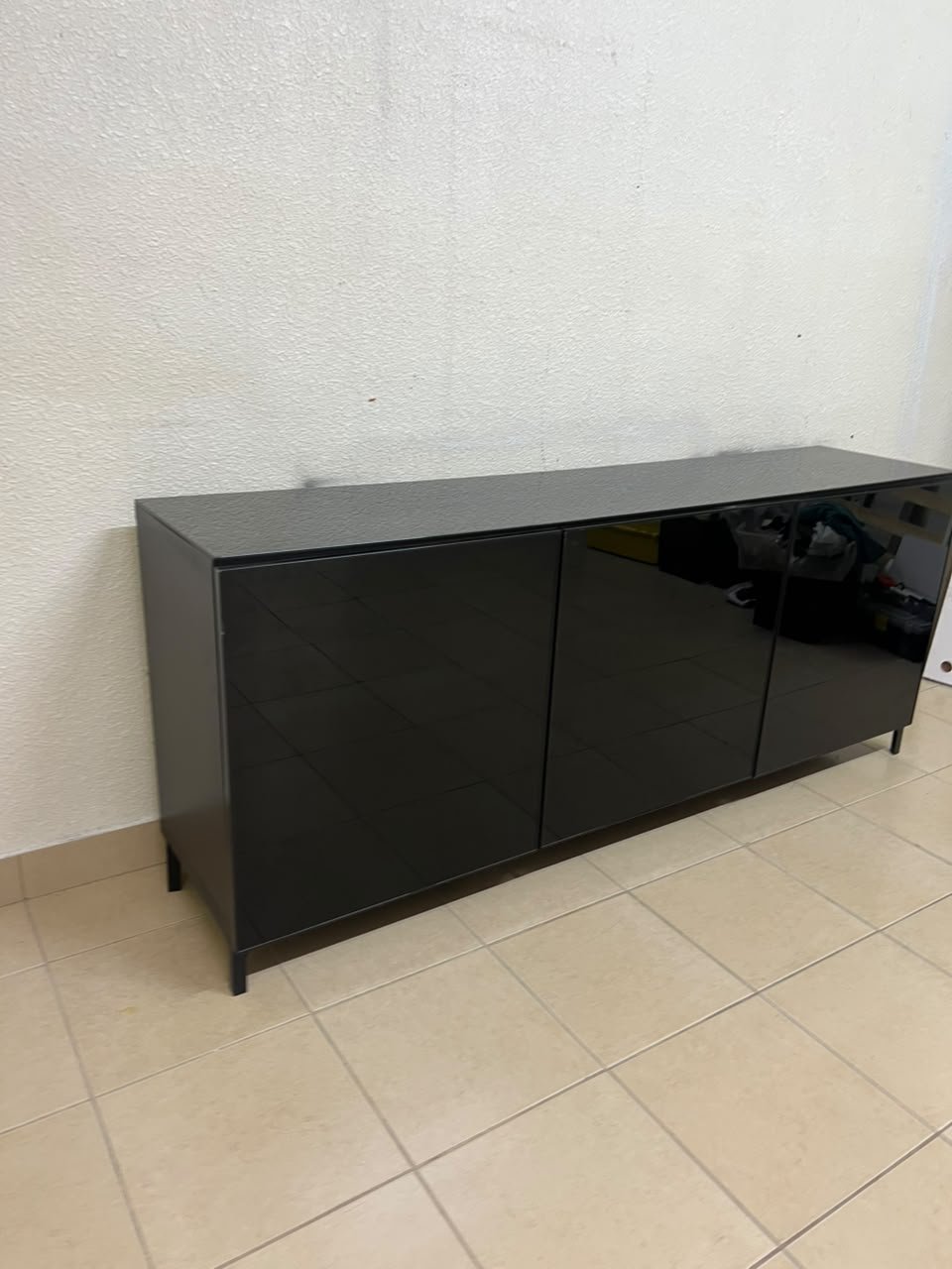 A cabinet (such as a TV stand or sideboard) that appears as a glossy black storage unit with three doors and slender legs; it bears a strong resemblance to the IKEA BESTÅ collection (specifically the Selsviken/Stubbarp combination in black-brown with high-gloss doors). - Image 5