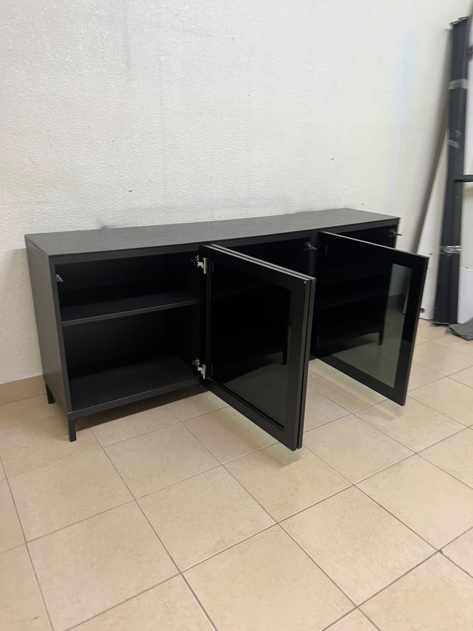 A cabinet (such as a TV stand or sideboard) that appears as a glossy black storage unit with three doors and slender legs; it bears a strong resemblance to the IKEA BESTÅ collection (specifically the Selsviken/Stubbarp combination in black-brown with high-gloss doors). - Image 8