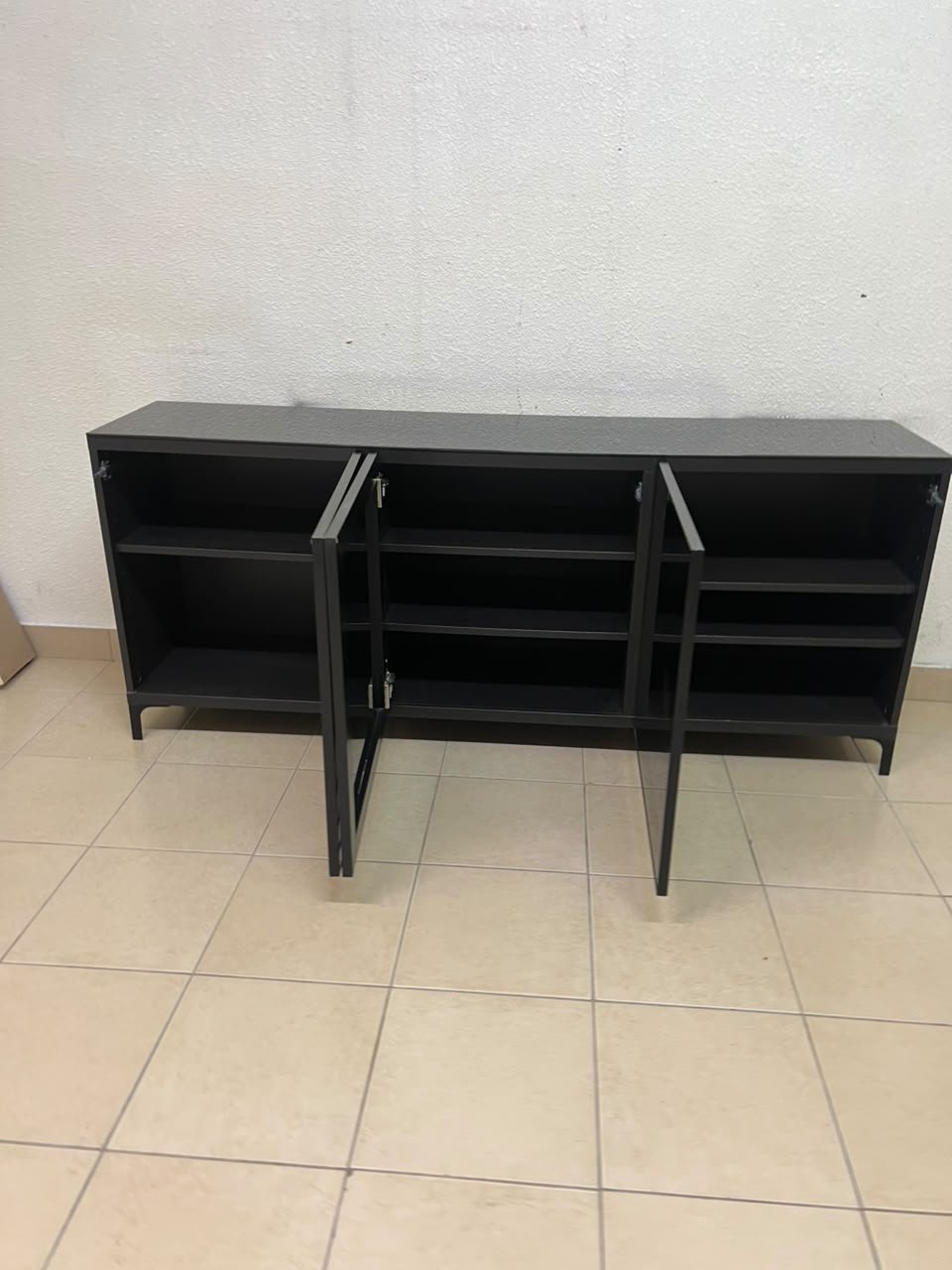 A cabinet (such as a TV stand or sideboard) that appears as a glossy black storage unit with three doors and slender legs; it bears a strong resemblance to the IKEA BESTÅ collection (specifically the Selsviken/Stubbarp combination in black-brown with high-gloss doors). - Image 10