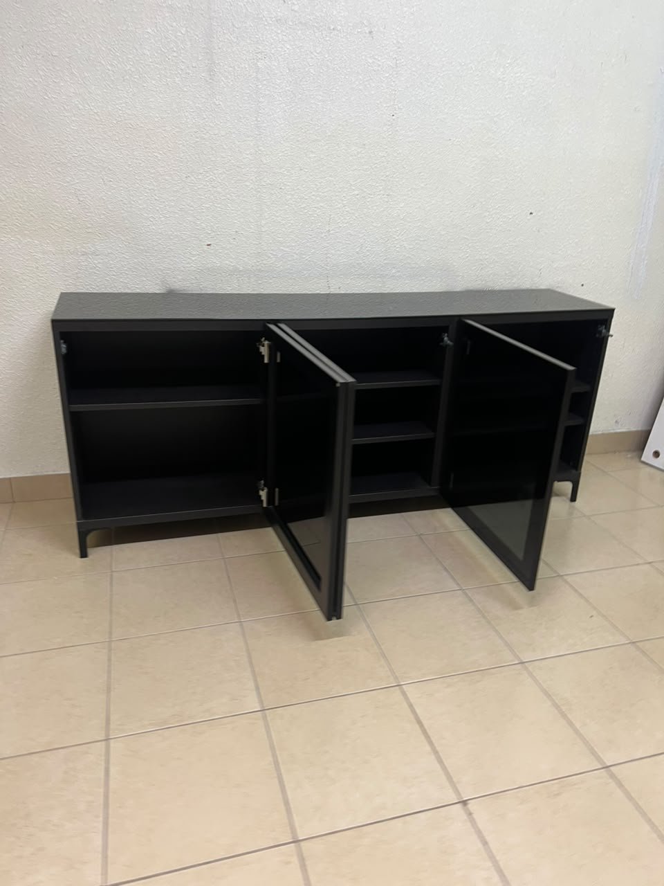 A cabinet (such as a TV stand or sideboard) that appears as a glossy black storage unit with three doors and slender legs; it bears a strong resemblance to the IKEA BESTÅ collection (specifically the Selsviken/Stubbarp combination in black-brown with high-gloss doors). - Image 12