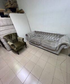 Classic Chesterfield-style furniture upholstered in velvet, featuring a long grey or silver sofa with a button-tufted backrest, accompanied by a matching armchair (fauteuil) in a dark green or olive shade, sharing the same plush, classic design.