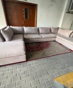 A U-shaped sectional sofa upholstered in beige or light gray fabric, featuring separate backrest cushions and two chaise longue/footrest sections on the sides.