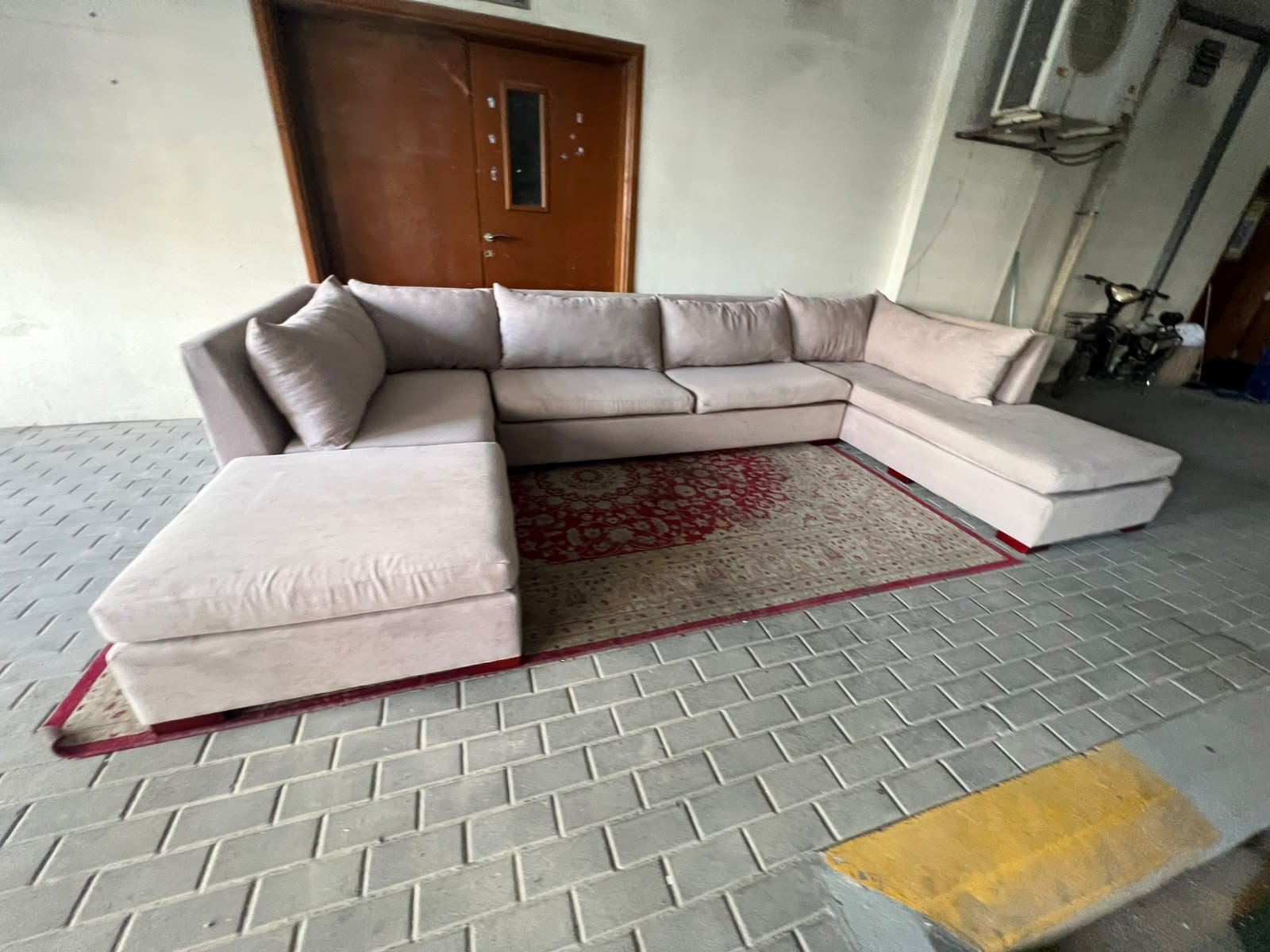 A U-shaped sectional sofa upholstered in beige or light gray fabric, featuring separate backrest cushions and two chaise longue/footrest sections on the sides.