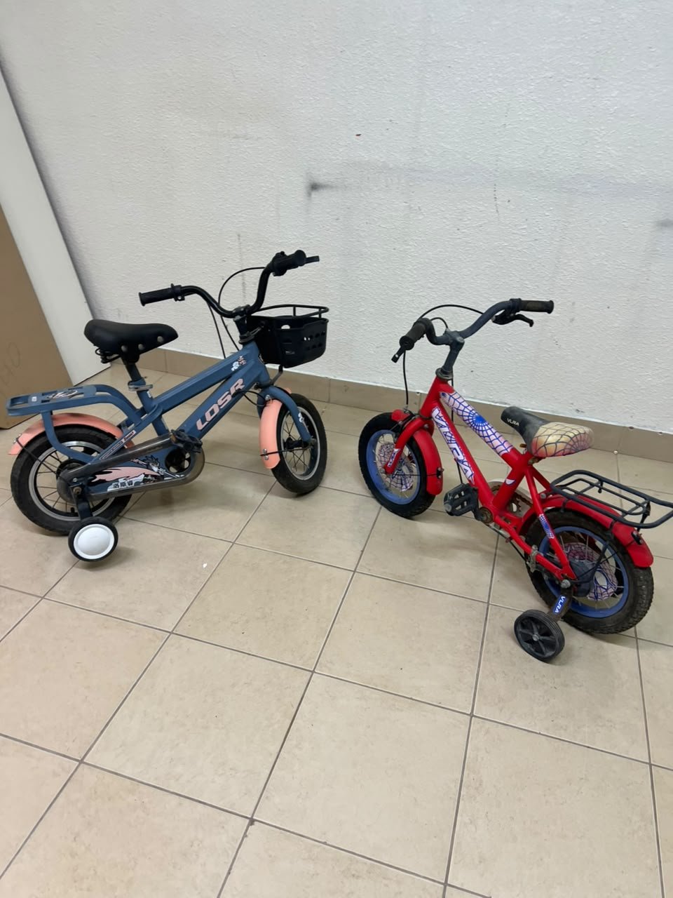 Two children’s bicycles in different colors (blue and red), equipped with training wheels and front baskets. - Image 8