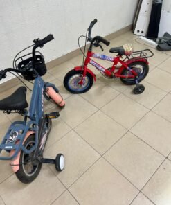 Two children’s bicycles in different colors (blue and red), equipped with training wheels and front baskets.