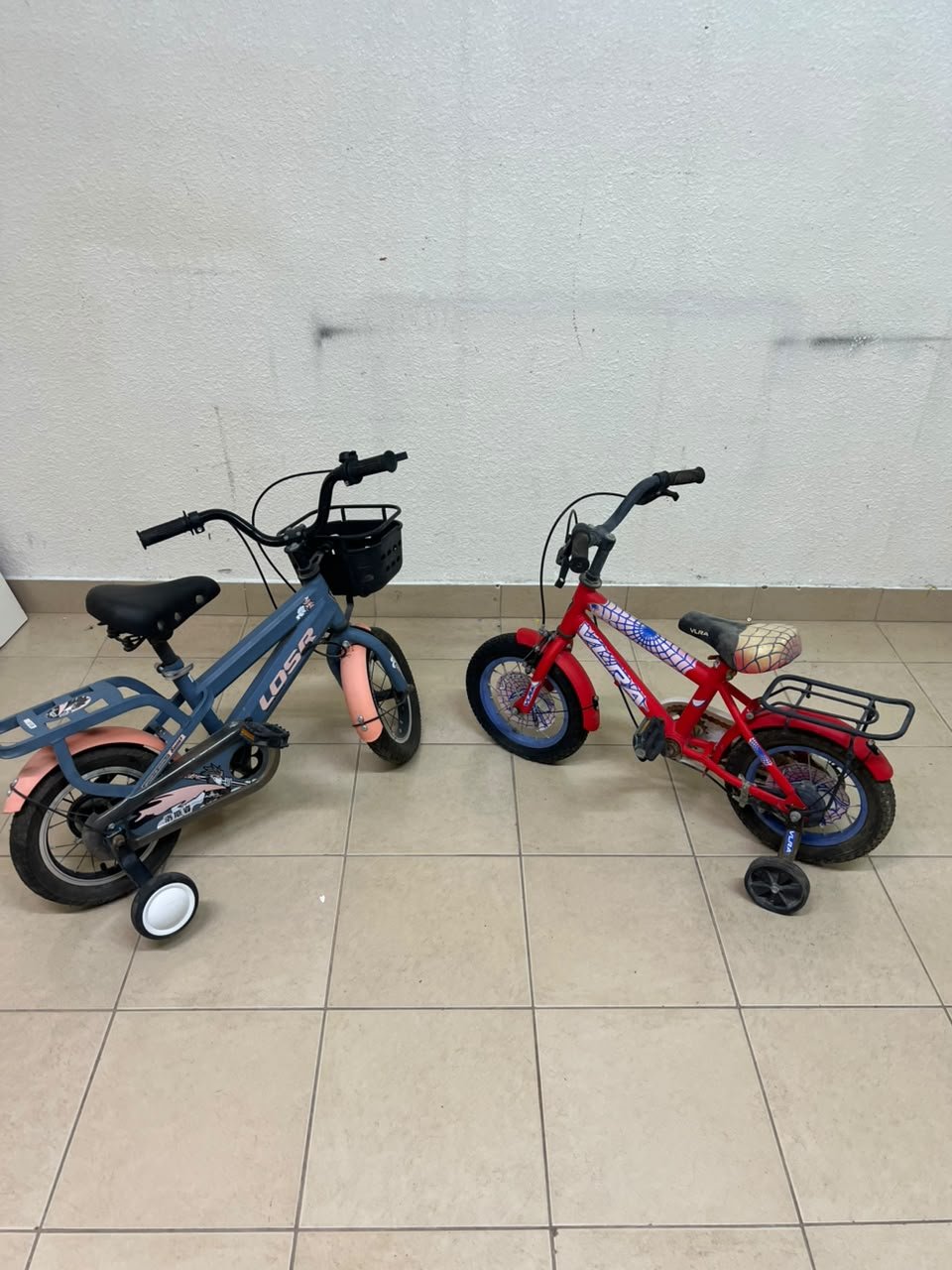 Two children’s bicycles in different colors (blue and red), equipped with training wheels and front baskets. - Image 2