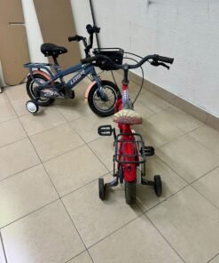 Two children’s bicycles in different colors (blue and red), equipped with training wheels and front baskets. - Image 3