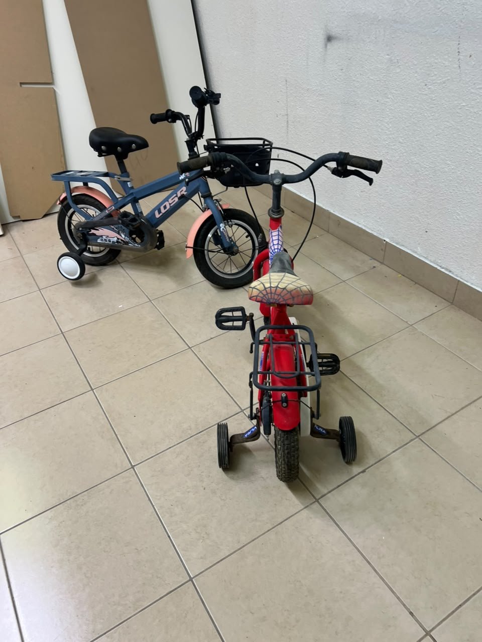 Two children’s bicycles in different colors (blue and red), equipped with training wheels and front baskets. - Image 3