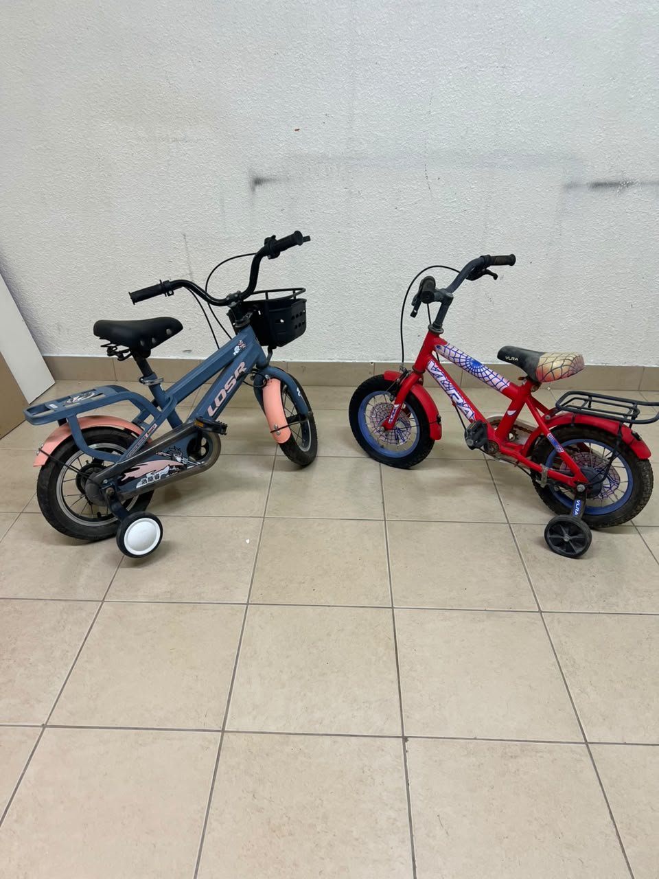 Two children’s bicycles in different colors (blue and red), equipped with training wheels and front baskets. - Image 4