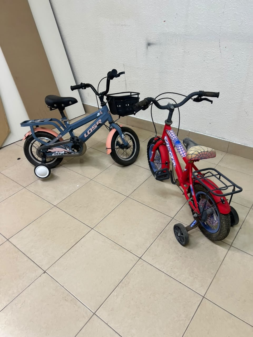 Two children’s bicycles in different colors (blue and red), equipped with training wheels and front baskets. - Image 5