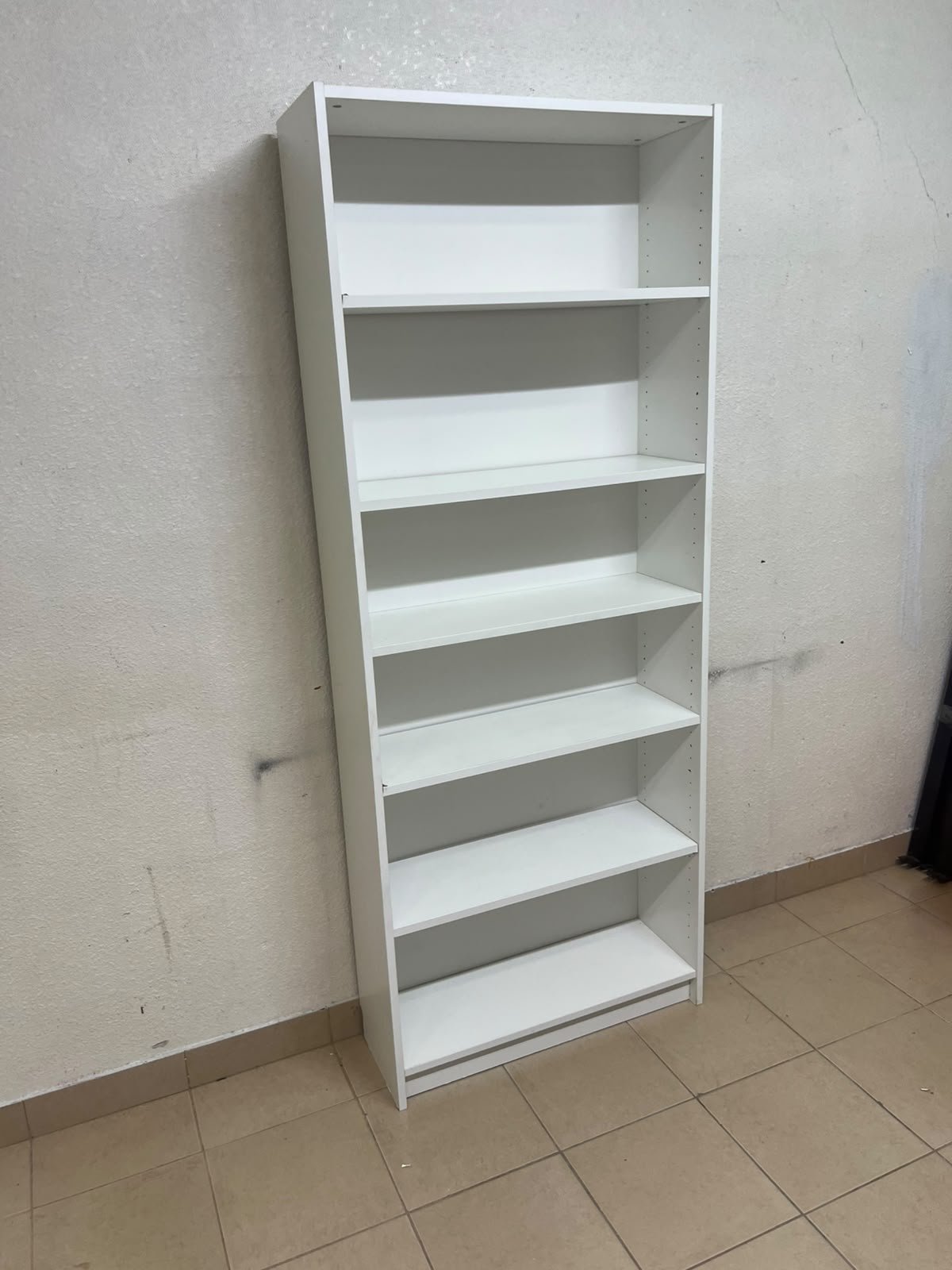 A white bookcase that looks similar to an IKEA BILLY bookcase or other comparable multi-shelf storage units.