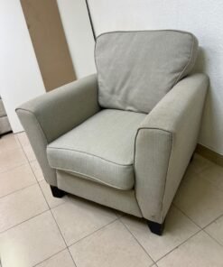 A single-seater fabric armchair in beige or light gray, featuring a separate seat cushion and back cushion, along with small black legs.