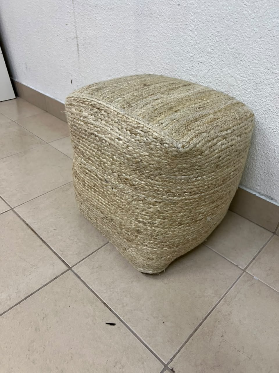 A square-shaped pouf made from braided natural jute fibers.