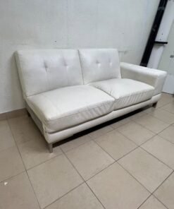 A white faux-leather sofa with a modern design, featuring button-tufted back cushions and slender metal legs.