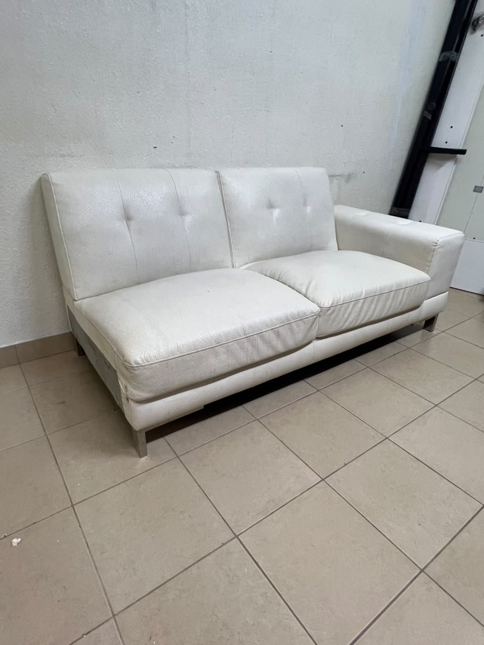 A white faux-leather sofa with a modern design, featuring button-tufted back cushions and slender metal legs.