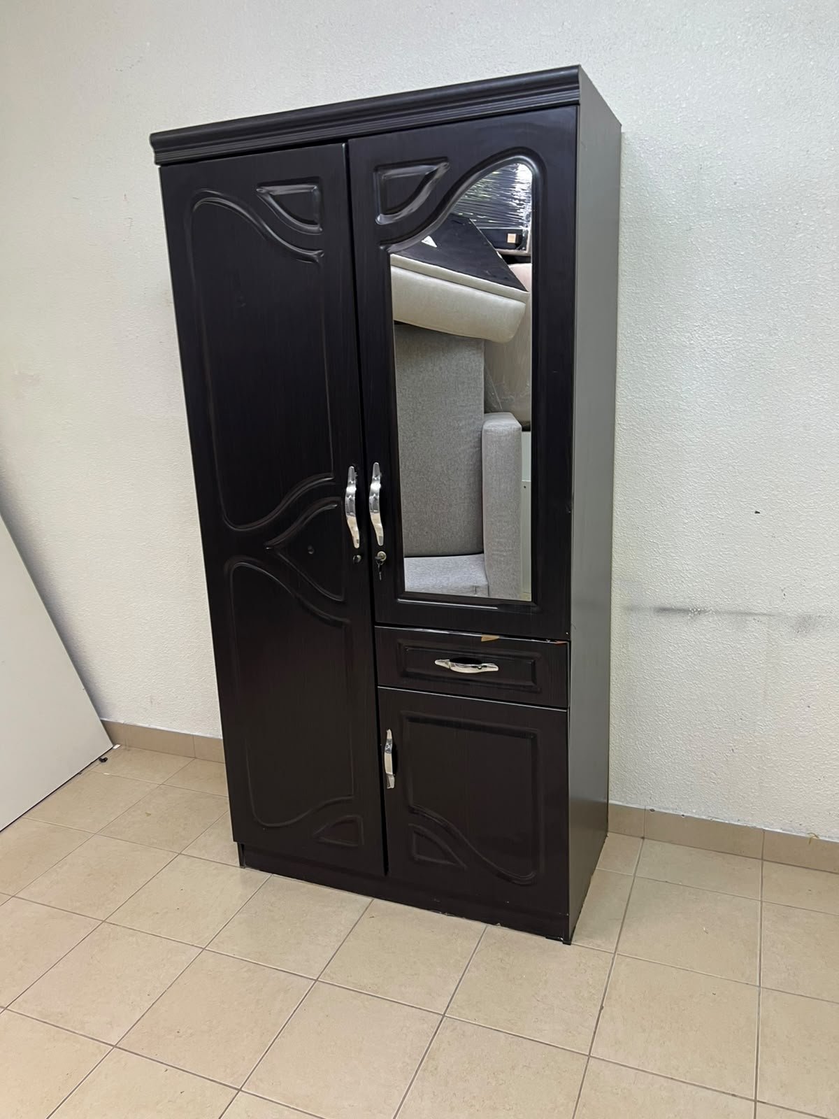 A dark brown (wenge-colored) wooden wardrobe featuring two doors—one of which has an upper mirror—along with a central drawer and a small cabinet (door) at the bottom.